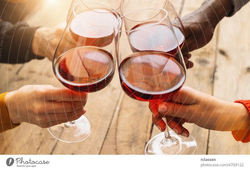 Hände, die auf ein Rotweinglas anstoßen, und Freunde, die sich bei einer Weinprobe amüsieren - Junge Leute genießen die gemeinsame Zeit bei einer Weinverkostung - Konzept der Jugend und Freundschaft