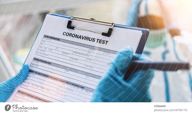 Ein Arzt füllt für einen Patienten in Schutzkleidung in einer Klinik, die sich an die Covid-19-Coronavirus-Epidemie anlehnt, ein Datenblatt für einen Coronavirus-Test mit einem Stift aus
