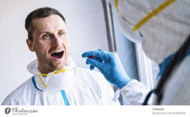 Medizinisches Fachpersonal in Schutzkleidung entnimmt einem erschöpften Kliniker in einem Covid-19-Testzentrum während einer Coronavirus-Epidemie ein Abstrichröhrchen aus dem Mund. Ablauf des PCR-DNA-Testprotokolls.