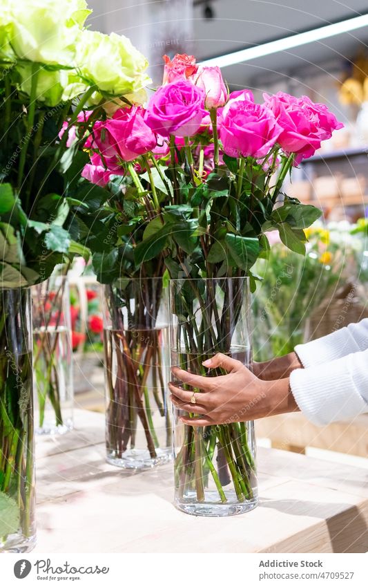Unbekannter Verkäufer stellt Vase mit Rosen auf den Tisch Arbeiter Roséwein Blumenladen Blumenstrauß Blumenhändler Pflanze Floristik Schürze Blütezeit