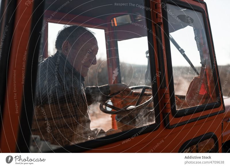 Alter Mann fährt Traktor auf einem ländlichen Feld Senior Landwirt Laufwerk Karre Schonung Ackerbau Landschaft männlich Baum führen Ernte Arbeit alt Vorstadt