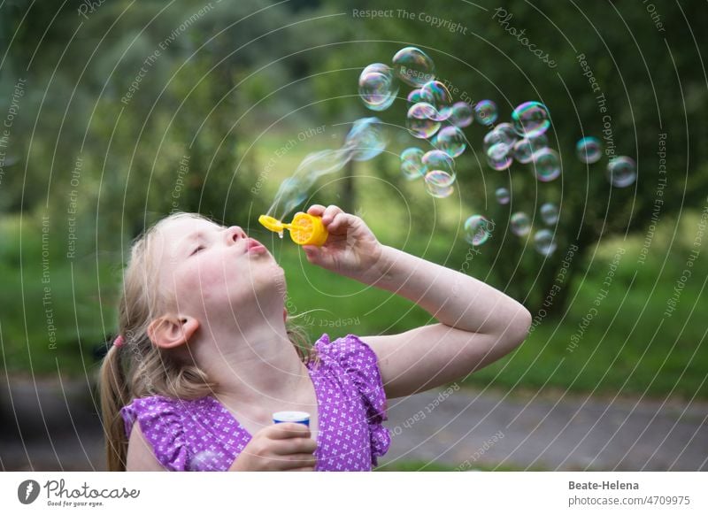 Junges Mädchen bläst Seifenblasen in das sommerliche Grün Sommer Sommerkleid Freude spielerisch Natur Glitzern Glück Kindheit Spielen Fröhlichkeit Spaß