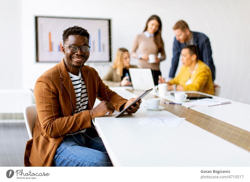Junger afroamerikanischer Geschäftsmann, der vor seinen Mitarbeitern im Sitzungssaal mit einem digitalen Tablet arbeitet schwarz Brainstorming Business