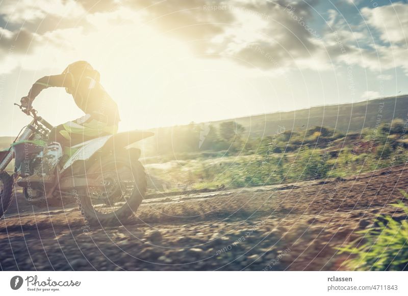 Motocross MX-Pilot in einer Kurve bei Sonnenuntergang auf einer Schotterpiste extrem Fahrrad enduro Rallye Dirtbike Staubwischen Schmutz Bahn Reiter