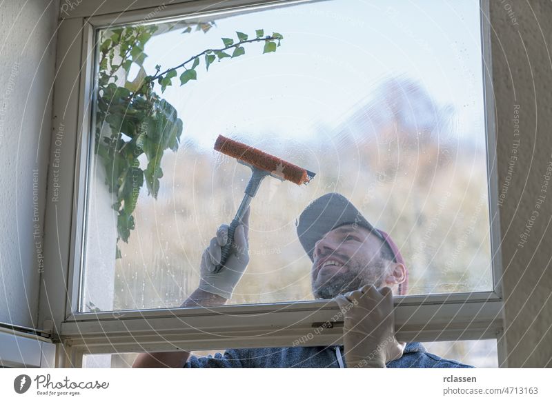 ein junger Mann benutzt einen Lappen und einen Abzieher beim Fensterputzen. professioneller Fensterputzer Pflege Sauberkeit Konzept Schmutz Spülmittel