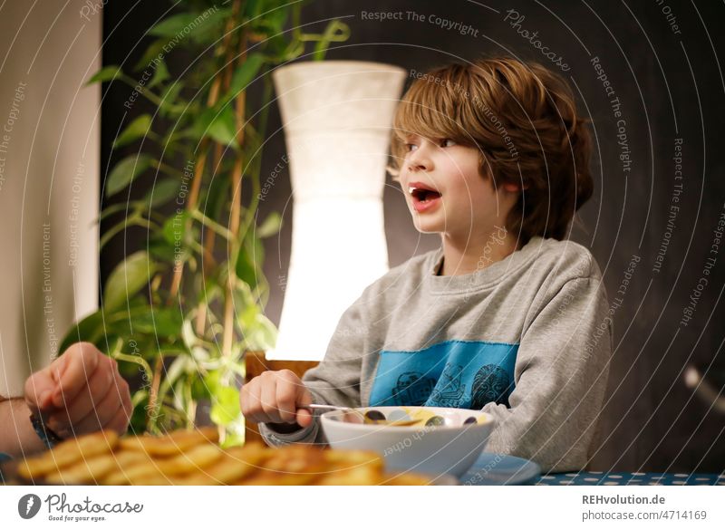 Kind erzählt beim Abendessen Essen gespräch Schulkind Esstisch Küche Lebensmittel Ernährung Junge Kindheit Porträt Tisch Schalen & Schüsseln Löffel Erziehung