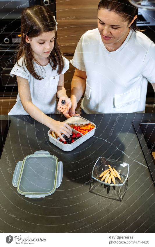 Mutter beobachtet, wie ihre Tochter das Essen in ihre Lunchbox packt Platzierung Blaubeeren Lunch-Box Schule gesunder Snack organisch Veganismus vorbereitend
