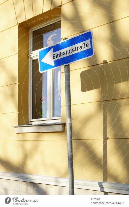 Verkehrsschild  - Einbahnstraße linksweisend -  und dessen Schatten an einem Wohnhaus mit Fenster und Mond  hinter der Glasscheibe / VZ 220-10 Verkehrszeichen