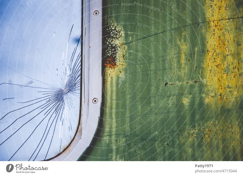 Detailaufnahme eines gesprungenen Fensters an einem alten Zugwaggon. Die Farbe blättert ab und zeigt Rostflecken. Waggon kaputt abblättern Menschenleer Verfall