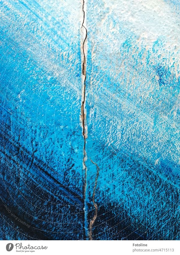 Ein langer Riss zieht sich durch die in verschieden blauen Schattierungen gestrichene Wand verputzt Putz dunkelblau hellblau weiß Mauer kaputt Fassade alt