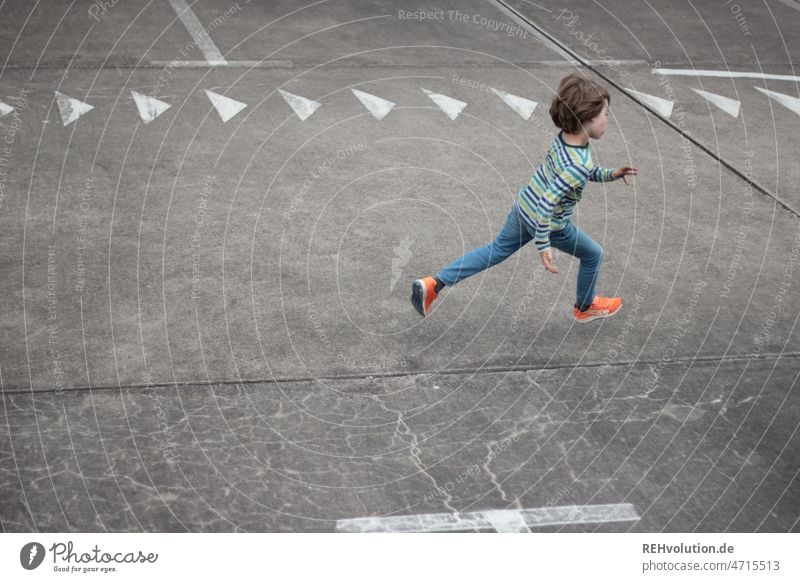 Kind rennt über einen Platz mit Pfeilen rennen Geschwindigkeit schnell Dynamik laufen Bewegung bewegen Kindheit sportlich Sport Spielen urban Stadt Parkplatz