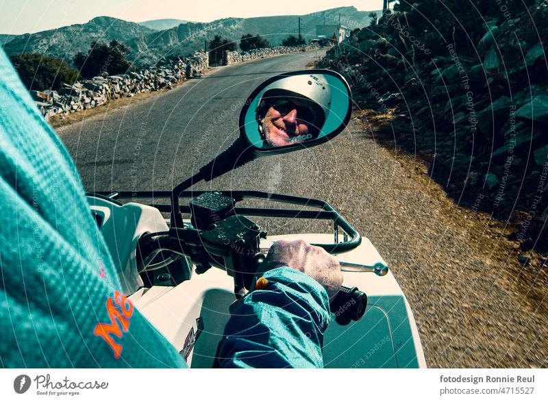 Quad-Fahrer mit Helm im Rückspiegel mit Hand am Gasgriff auf einer griechischen Straße Gesicht Gashand Mann 50 bis 60 Jahre alt Lächeln Erwachsener Spaß Freude