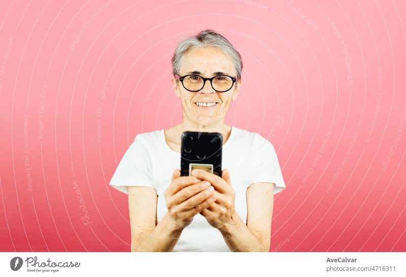 Alte Frau überprüft sein Smartphone glücklich, während lächelnd, was eine Warnung posiert isoliert über rosa Farbe Wand Hintergrund. Tägliche Ausdrücke mit Kopie Raum im Studio.