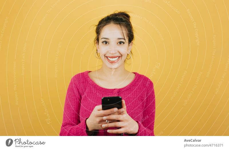 Junge afrikanische Frau Überprüfung glücklich sein Smartphone erhalten gute Nachrichten posiert isoliert über gelbe Farbe Wand Hintergrund. Tägliche Ausdrücke mit Kopie Raum im Studio.