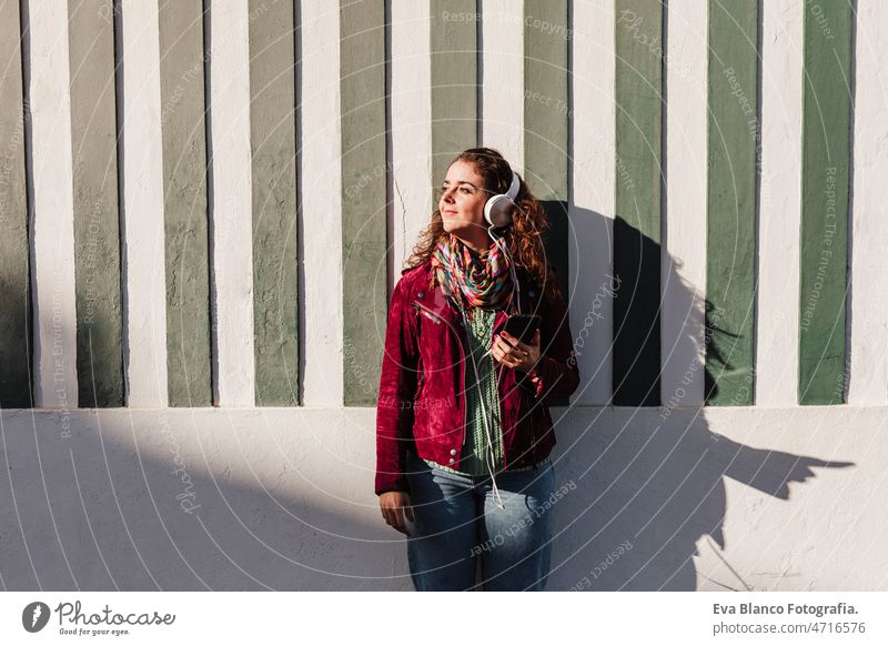 entspannte Frau hört Musik über Kopfhörer.bunte Häuser.Promenade Costa Nova, Aveiro, Portugal hören Großstadt sonnig 30s Kaukasier Glück Headset Handy