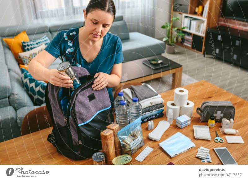 Frau stellt Dosen mit Lebensmitteln für einen Notfallrucksack bereit Setzen Rucksack vorbereitend Notfalltasche 72 Stunde Notfallevakuierung Katastrophenschutz