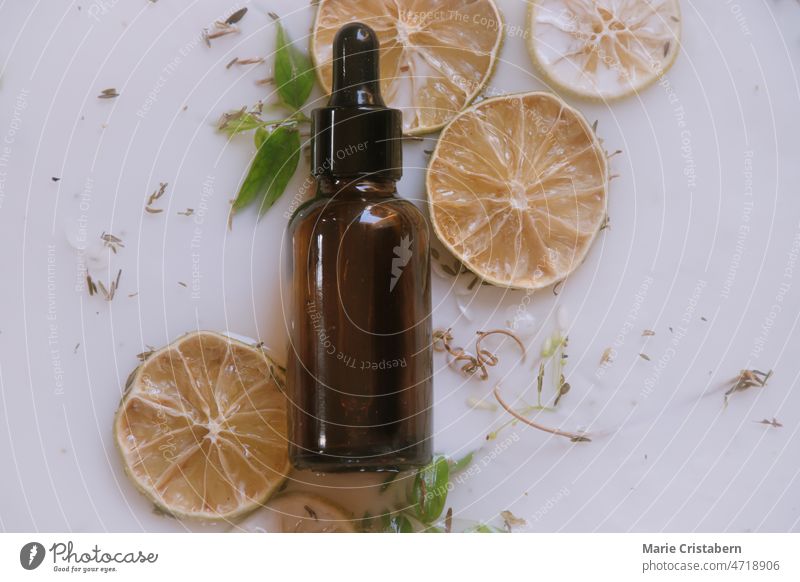 Produktfoto einer Glastropfenflasche mit einem natürlichen Anti-Aging-Serum vor einem aromatischen Milchbad mit getrockneten Zitrusfrüchten und Kräutern Glamour