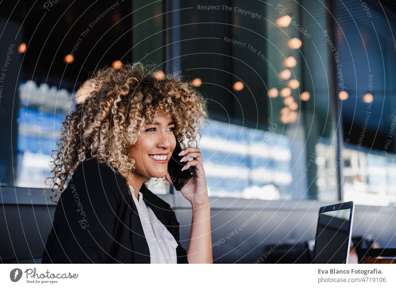 Lächelnde hispanische Geschäftsfrau in einem Café, die an einem Laptop und einem Mobiltelefon arbeitet. Technik und Lifestyle Computer Afro-Look Frau Business