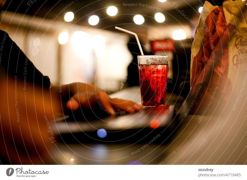 Selektiver Fokus von Erdbeer-Tee-Eis-Getränk mit unscharfer Hand Freiberufler arbeiten am Laptop in der späten Nacht im Café Person Computer Business Arbeit