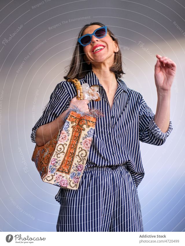 Fröhliche Frau mit Sonnenbrille und Tasche Stil Mode Outfit feminin Design Kleidung Stilrichtung Vorschein Raum Bekleidung trendy Kleidungsstück Accessoire Wand