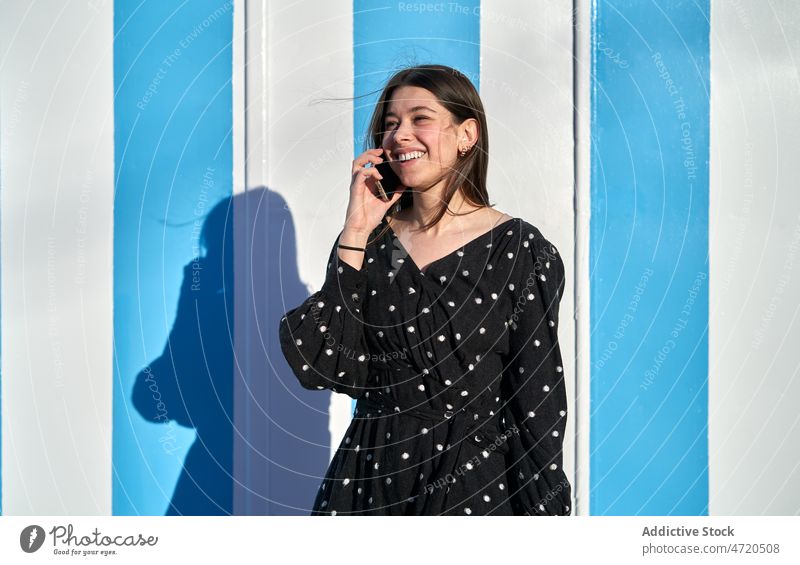 Lächelnde Frau in der Nähe einer mehrfarbigen Wand reden Telefon Smartphone Mobile Straße Stil feminin Mode Outfit Freizeit Bekleidung heiter Sommer jung