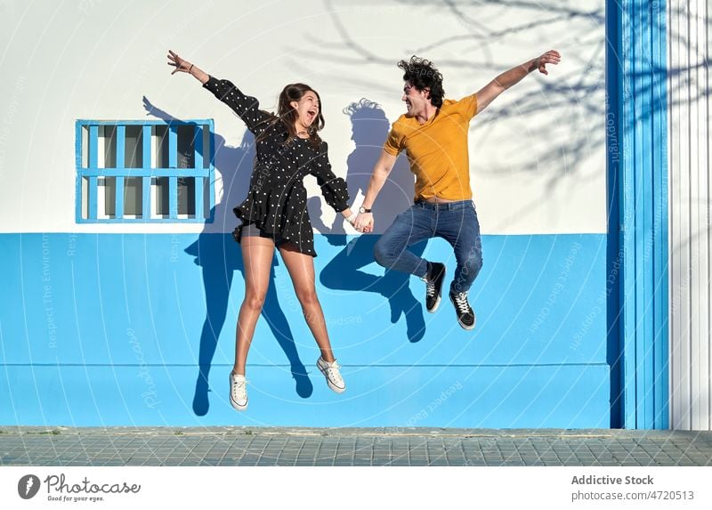 Fröhliches Paar springt in der Nähe der Mauer springen Spaß haben Aktivität Partnerschaft Wand Liebe Straße Freizeit Bonden Zuneigung Zusammensein jung Glück