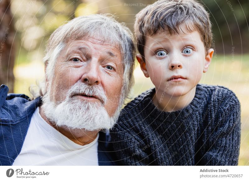 Positiver älterer Großvater, der in die Kamera schaut, und Enkel mit Glotzaugen Porträt Junge Mann Grimasse Gesicht machen positiv Kind Aussehen wenig männlich