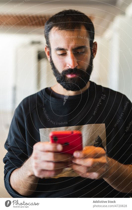 Bärtiger Mann im Sweatshirt surft auf seinem Smartphone benutzend Textnachricht online Surfen prüfen lesen Internet Apparatur männlich Texten modern lässig