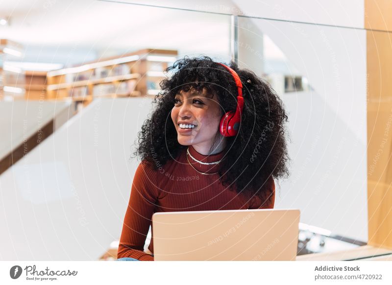 Erfreuliche afroamerikanische Frau hörte Musik vom Laptop Bibliothek benutzend meloman Schüler Kopfhörer Lächeln Browsen zuhören Bildung genießen ethnisch Glück