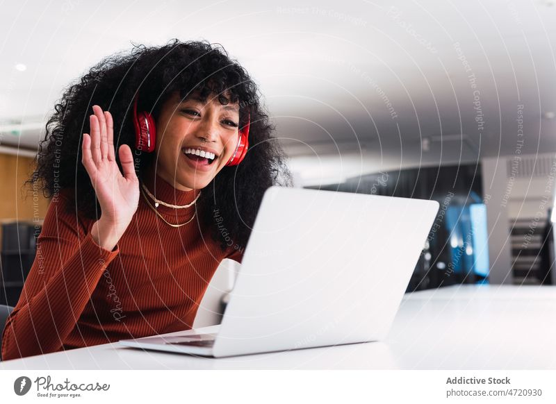 Ethnische Frau mit Laptop, die während eines Videoanrufs eine Grußgeste zeigt Hallo Wellenhand Hi gestikulieren benutzend Kopfhörer Lächeln Browsen genießen