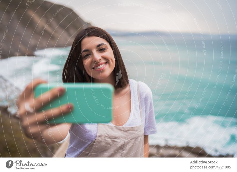 Fröhliche Frau, die ein Selfie am Meeresufer macht MEER Ufer Küste Zeitvertreib Ausflug Smartphone Fotografie einfangen Gedächtnis Selbstportrait Freizeit