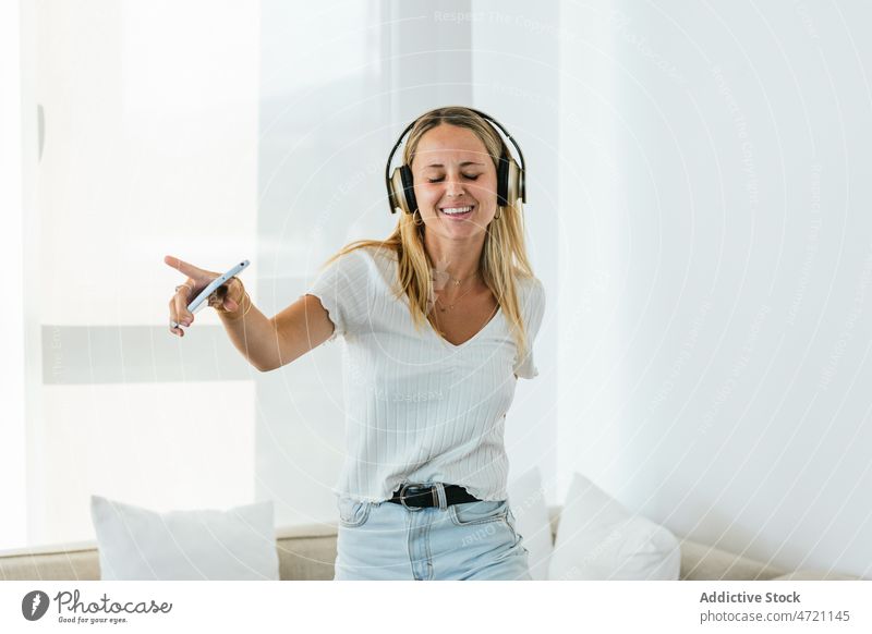 Fröhliche Frau, die mit Kopfhörern Musik hört Wohnzimmer meloman Wiedergabeliste Gesang Hobby Melodie genießen zuhören Smartphone heimwärts Drahtlos heiter