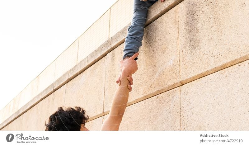 Crop Person hält die Hand eines Mannes auf einem Gebäude Dach stark Zusammensein Hilfsbereitschaft Athlet Händchenhalten Verschluss Griff abstützen Le Parkour