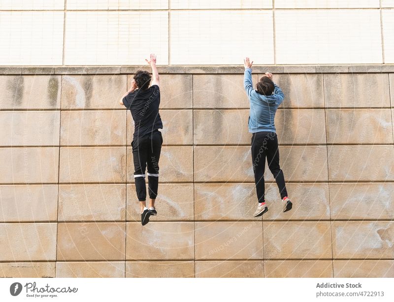 Zwei anonyme Athleten, die einen Sprung auf ein Dachgebäude wagen Mann springen Training Gebäude Arme hochgezogen Wand passen Straße Aktivität männlich Typ