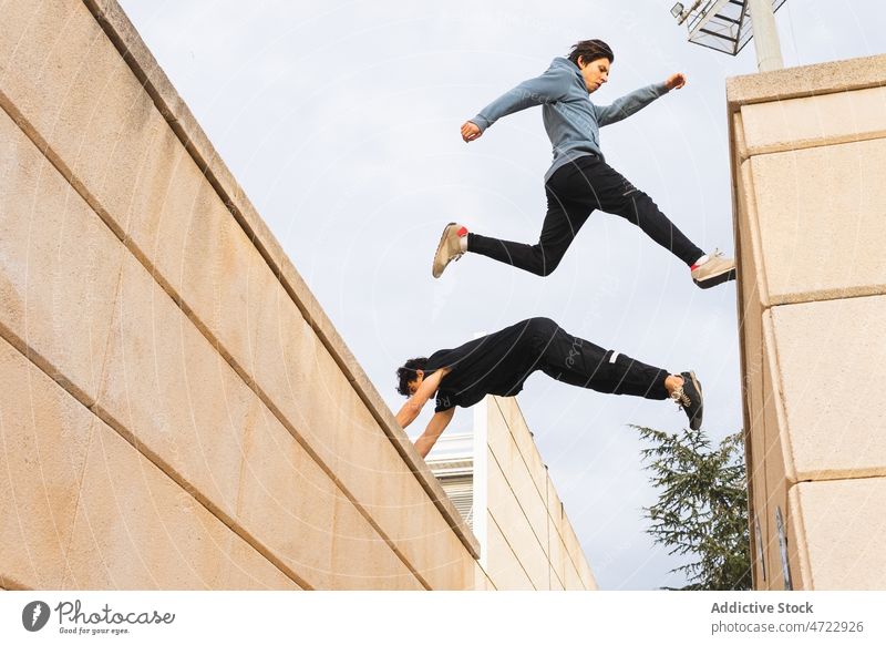 Starke Männer springen auf ein Hausdach in der Stadt Mann Le Parkour Dach Training extrem aktiv Straße Großstadt Borte männlich Typ Sprung Trick unkenntlich