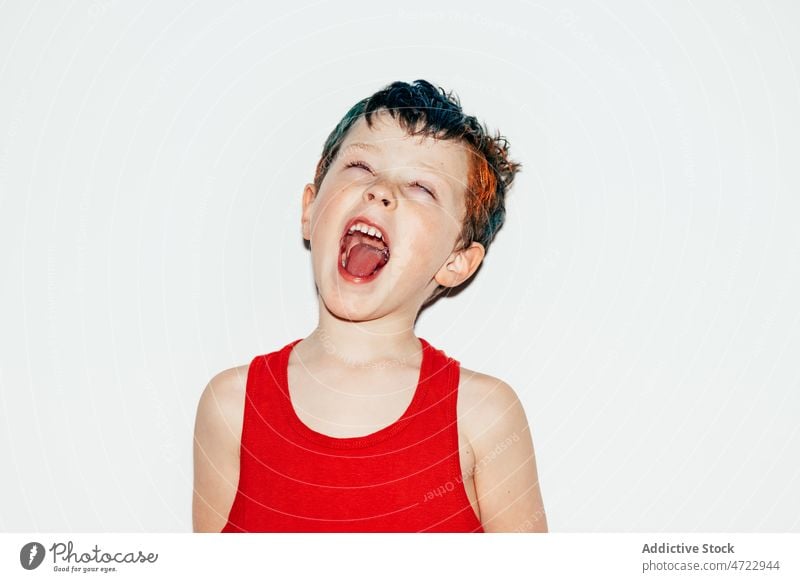 Ungezogener Junge zeigt Zunge Kind unanständig schelmisch rebellisch schreien ungehorsam widerspenstig Raum Porträt offener Mund rollende Augen Licht farbenfroh
