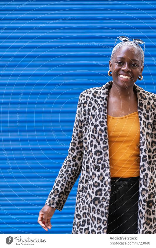 Positive schwarze Frau in der Nähe der blauen Wand Straße Stil Vorschein Outfit trendy Großstadt urban Kleidungsstück Lächeln Afroamerikaner froh Inhalt Glück