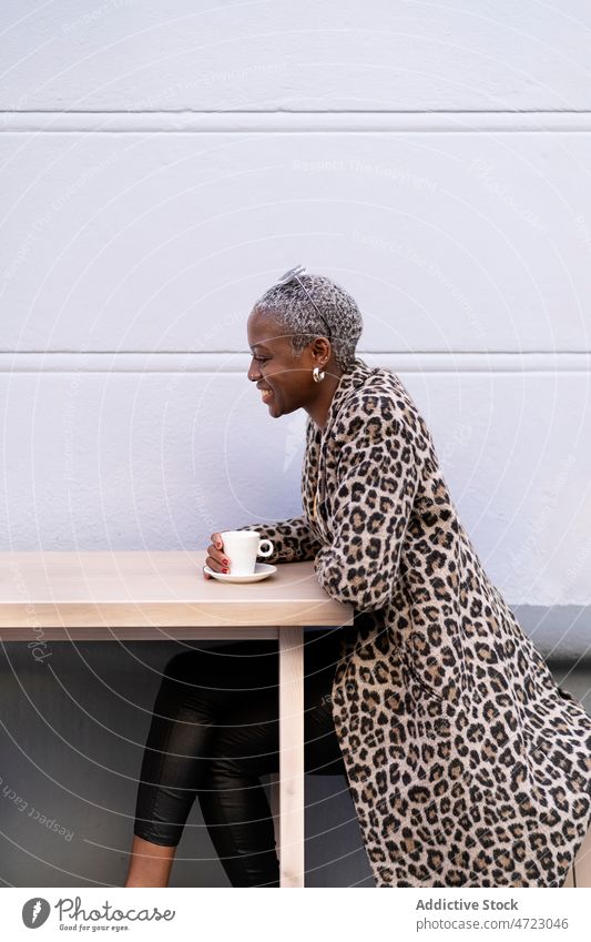 Optimistische schwarze Frau in einem Straßencafé Café Terrasse Kaffeepause spielerisch Zeitvertreib Handarbeit Vorschein Afroamerikaner Kurze Haare Großstadt