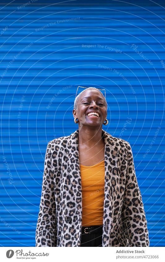 Positive schwarze Frau in der Nähe der blauen Wand Straße Stil Vorschein Outfit trendy Großstadt urban Kleidungsstück Lächeln Afroamerikaner froh Inhalt Glück
