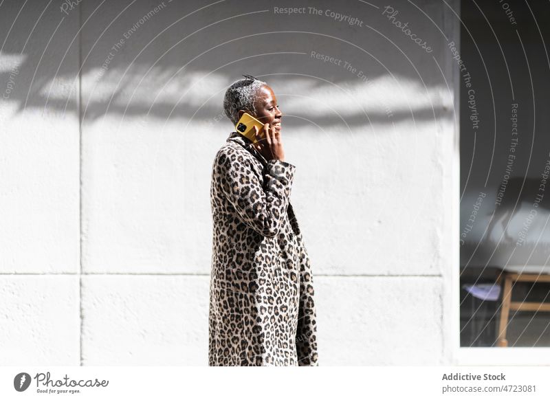 Stilvolle schwarze Frau, die in der Stadt mit ihrem Smartphone chattet Straße Telefonanruf Gespräch diskutieren Kommunizieren Talkrunde Großstadt trendy Outfit