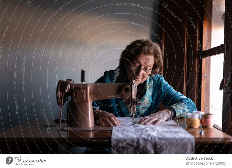 Ältere Frau näht an einer Maschine Nähmaschine Nähen Textil Näherin Basteln Hobby Vorrichtung Faser Instrument Stil Garn Design Raum Handwerkerin Tisch