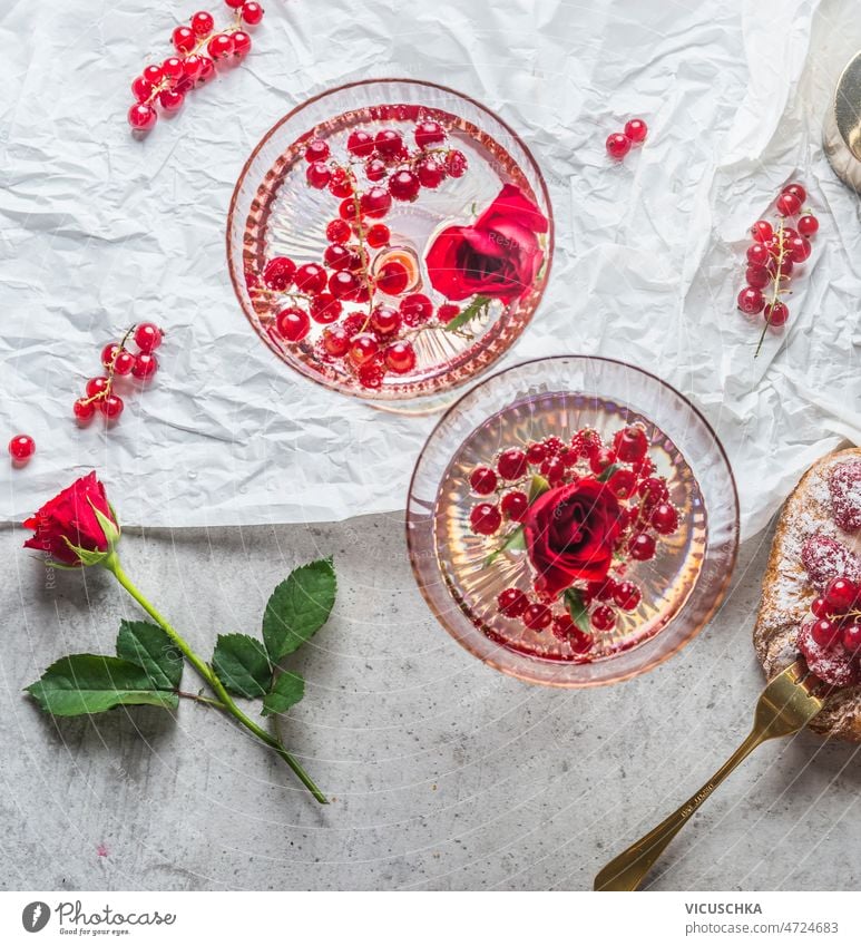 Nahaufnahme von zwei Sektgläsern mit roten Johannisbeeren und Rosenblüten abschließen Champagnergläser rote Johannisbeeren Roséwein Blütenblätter weiß Tisch