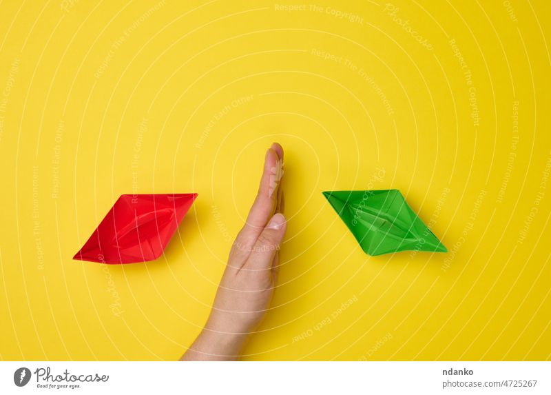 weibliche Hand zwischen Papierbooten auf gelbem Hintergrund, das Konzept der Versöhnung der Parteien, die Suche nach Kompromissen. Die Rolle des Unterhändlers im Dialog