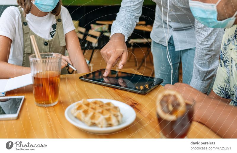 Unbekannte Freunde benutzen Tablet in einem Café unkenntlich Kaffeehaus Tablette Hand Coronavirus Schutzmaske Kantine Detailaufnahme Tisch Zeigen Buchung