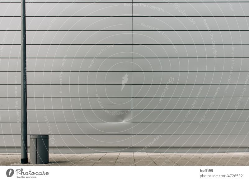 Eine Delle in der Fassade mit Laternenpfahl und Mülleimer minimalistisch Wand Metallfassade Abdruck eingedrückt beschädigung grau Strukturen & Formen Linie