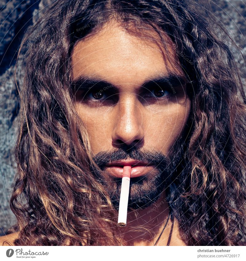 Porträts eines 35 Jahre alten Mannes mit langen Haaren und cigarette Junger Mann lange Haare krause Haare Latin Lover erotisch Hippie selbstgenügsam Damenbart
