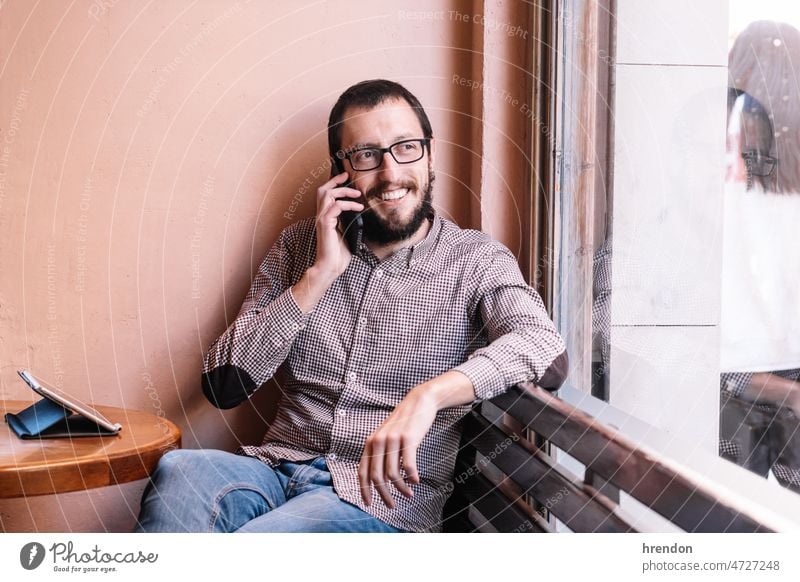 Junger kaukasischer Mann lächelt fröhlich und spricht mit dem Smartphone Handy Telefon sprechend Mitteilung Lächeln männlich im Innenbereich