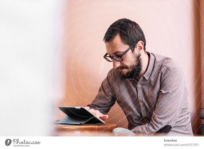 Junger Geschäftsmann arbeitet an seinem Tablet in einem Café Heimarbeitsplatz arbeiten junger Erwachsener Arbeiter Lebensstile Kleinunternehmen Laptop