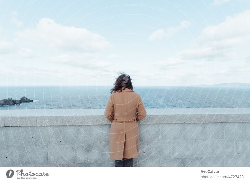 Junge Frau auf einem braunen Mantel, die zum Horizont schaut, Konzept der psychischen Gesundheit. Heller Himmel, Einsamkeit und Reflektion. Blick in die Zukunft