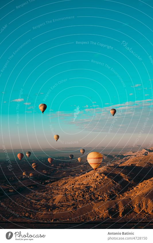 Erstaunliche vertikale Aufnahme von Dutzenden von Heißluftballons fliegen rund um die Luxor Ägypten Bereich. Wüste orange Bereich früh am Morgen. Hellblauer Himmel
